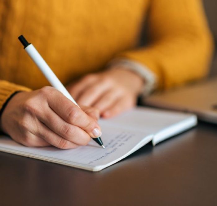 Close-up of a person writing in a notebook with a black pen regarding the difference between passed vs past