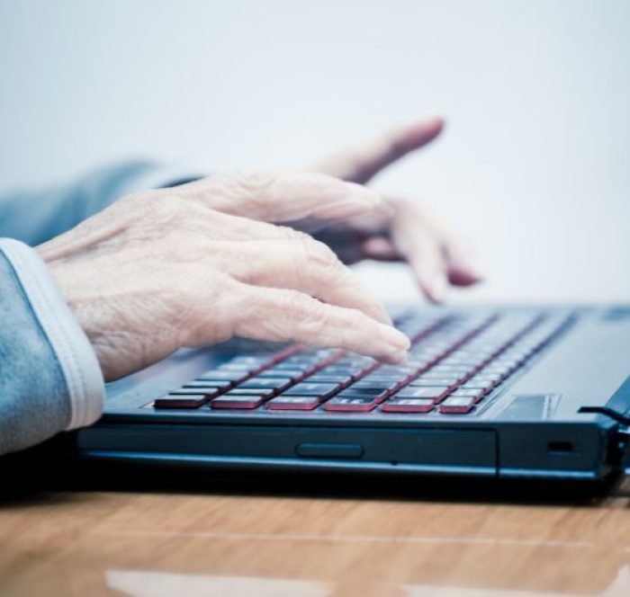 Hands typing on a laptop with red-backlit keys. The focus is on the fingers, conveying concentration and engagement with technology.