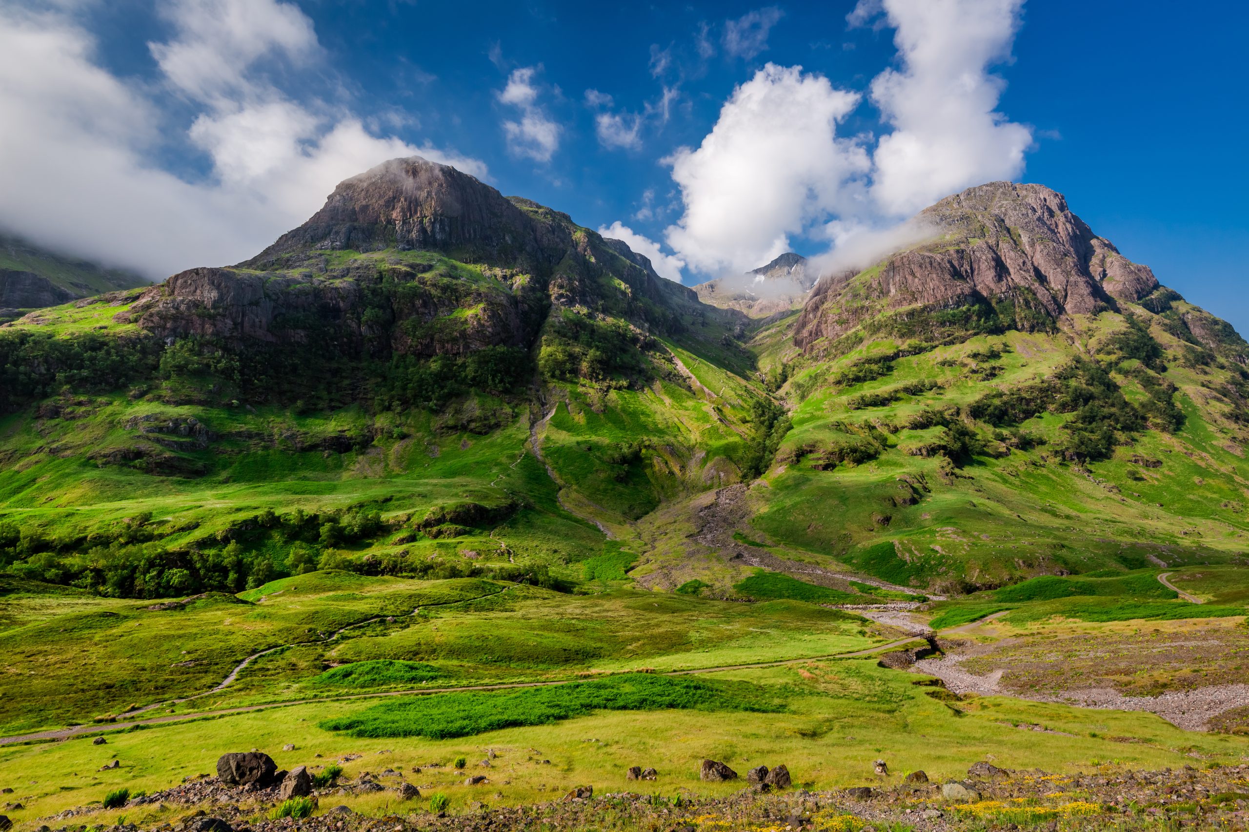 A stunning sunrise over the Mountains of Glencoe in summer, Scotland, with golden light illuminating the rugged peaks and lush green valleys.