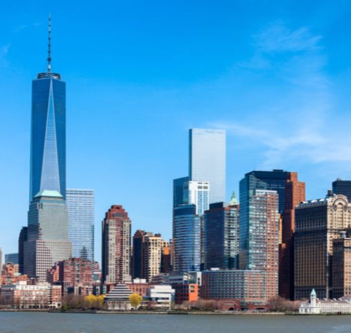 Skyline of New York City with One World Trade Center and surrounding skyscrapers under a clear blue sky, conveying a sense of urban grandeur.