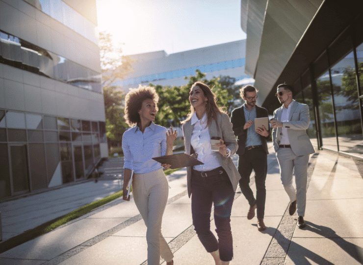 Business colleagues walking and smiling with each other outside a corporate office. Improve your Business English skills with Oxford International